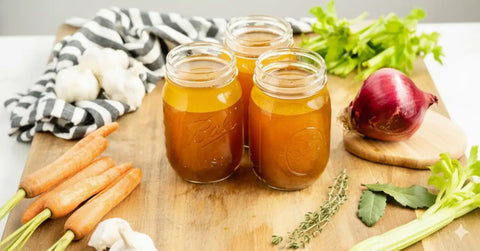 32-ounce glass mason jar filled with golden broth, surrounded by fresh vegetables.