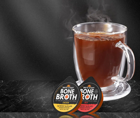 Bone broth cup and pod set, clear glass mug with handle, dark brown liquid inside, branded packaging for ’bone broth’ in white text on yellow background.