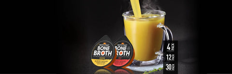 Bone broth mug with yellow liquid and straw, black background.